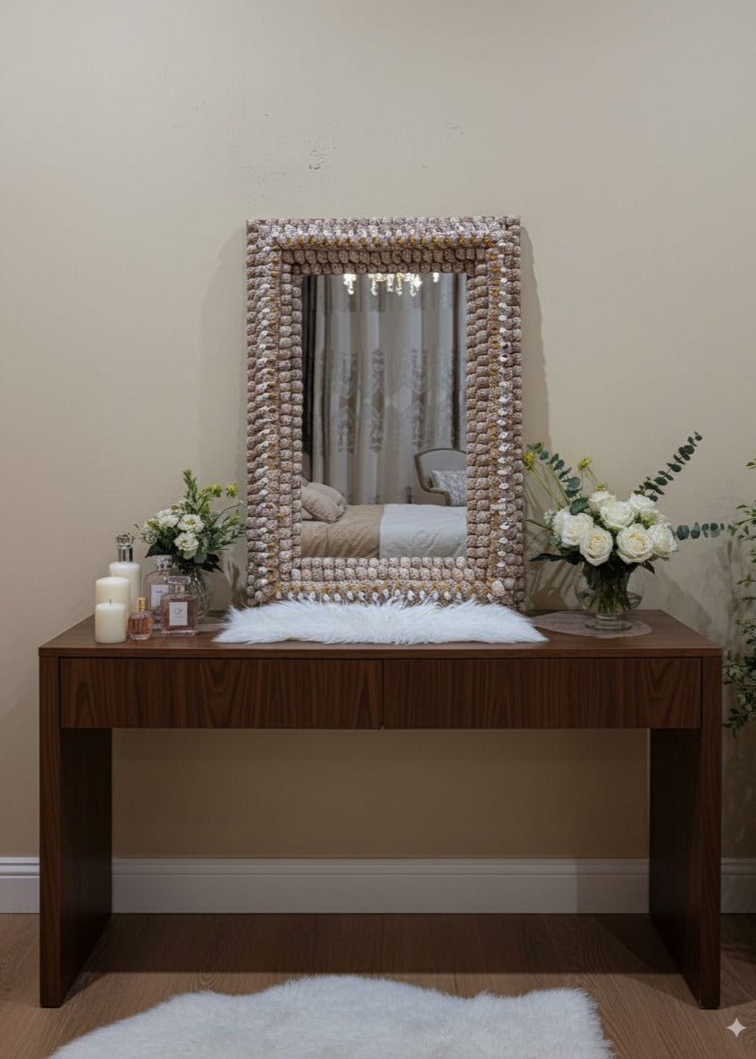 Wooden vanity table with decorative mirror and flowers against a beige wall.