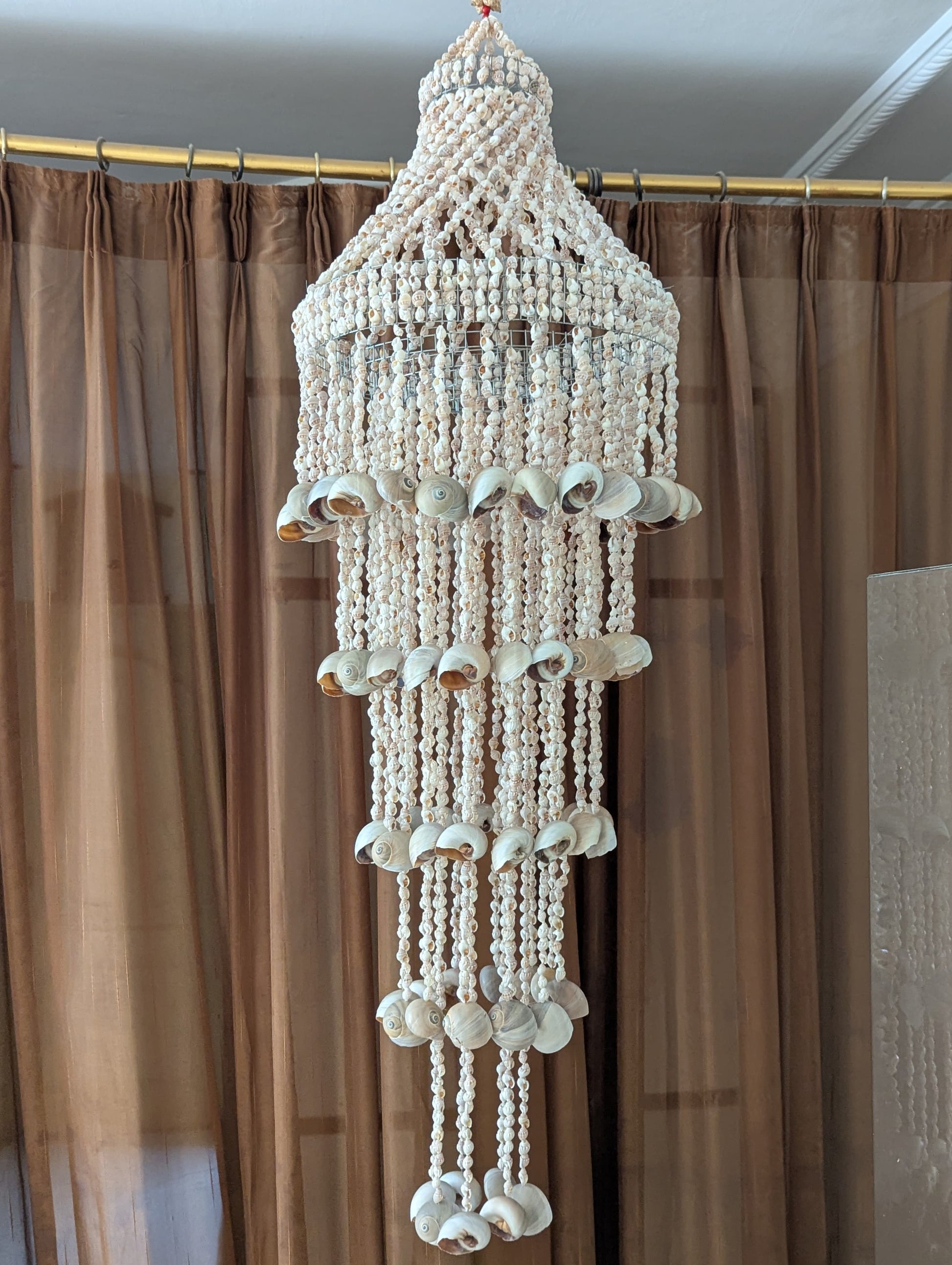 Decorative wall hanging with beads and shell-like elements against a brown curtain background