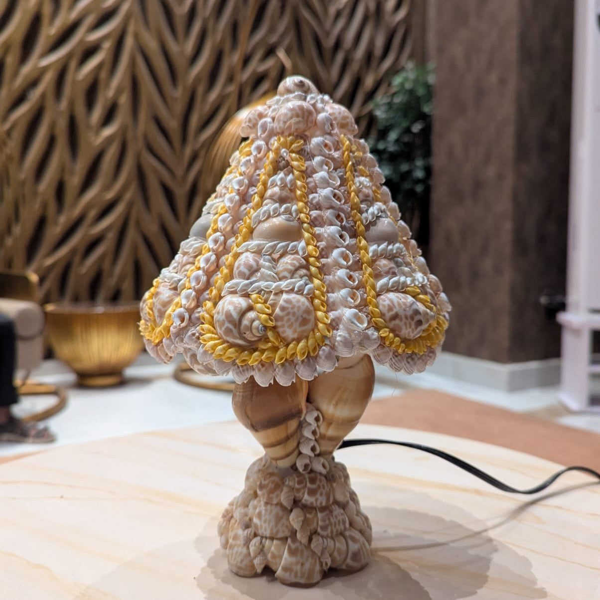 Decorative lamp made of seashells on a marble surface with a textured wall in the background.