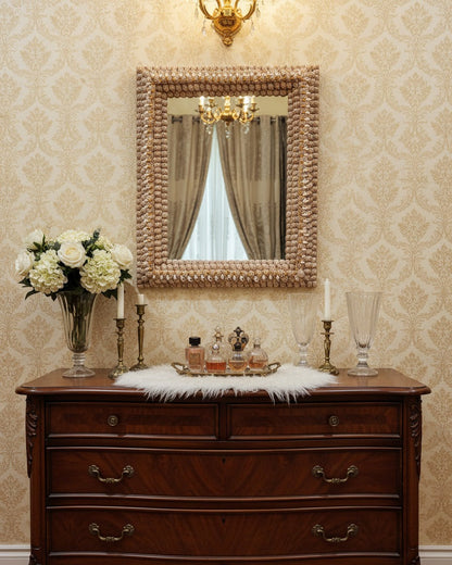 Wooden dresser with decorative mirror, flowers, and candles against a patterned wall.