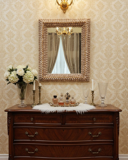 Wooden dresser with decorative mirror, flowers, and candles against a patterned wall.